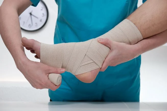 Nahaufnahme eines männlichen Arzt, der den Fuß eines Patienten bandagiert 