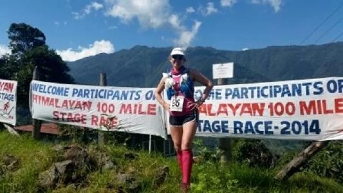 Bir kadın, "HIMALAYA 100 MİL ETAP YARIŞI - 2014'ÜN KATILIMCILARINA HOŞ GELDİNİZ" yazan bir pankartın yanında duruyor.